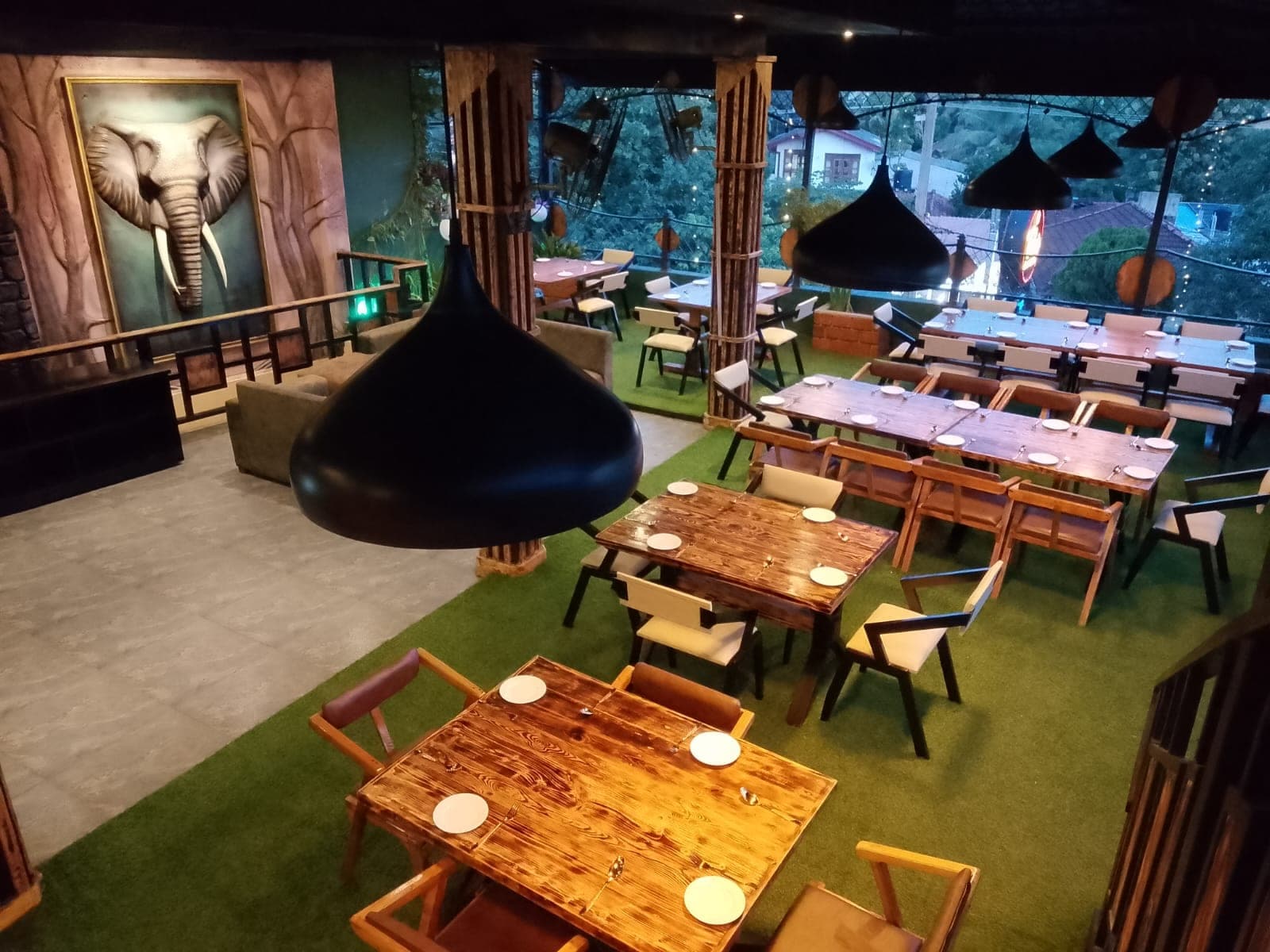 The upstairs lounge: wooden tables on green turf under black pendant lamps, with an elephant relief on the wall